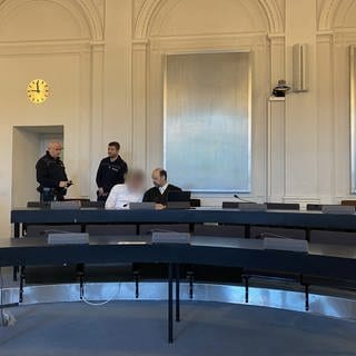 Der tatverdächtige Ehemann sitzt auf der Anklagebank am Landgericht Karlsruhe. Neben ihm sein Verteidiger und im Hintergrund sind zwei Justizbeamten zu sehen. Die Staatsanwaltschaft fordert eine lebenslange Gefängsnisstrage für den Angeklagten. Am Freitag soll das Urteil fallen.