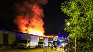 Hohe Flammen schlagen aus der Lagerhalle eines Möbelgeschäfts. Die Feuerwehr steht daneben und löscht den Brand im Kreis Karlsruhe.