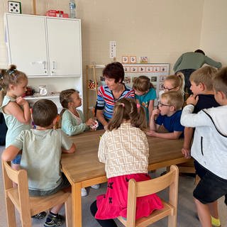 Viele Kinder sitzen rund um einen Tisch zusammen mit einer Erzieherin