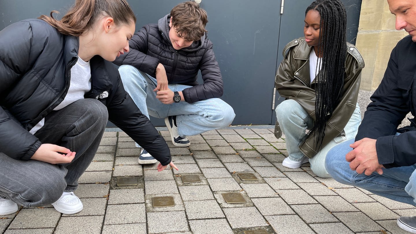 An einer Schule in Pforzheim erinnern sich Schülerinnen und Schüler an die Reichspogromnacht. Sie hocken im Kreis vor Stolpersteinen.
