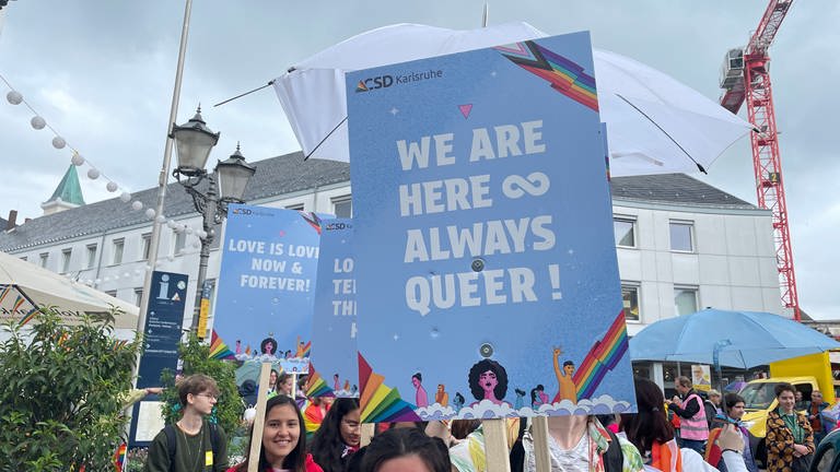 Ein Plakat mit dem Motto CSD 2024 in Karlsruhe bedruckt: "We are here, always queer!"