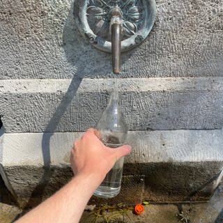 Eine Glasflasche auffüllen am Trinkwasserbrunnen