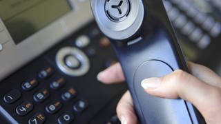 Ein Telefon wird abgehoben und liegt in der Hand.