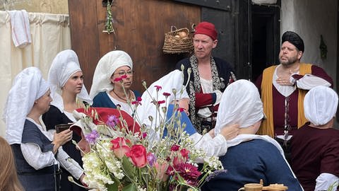 Mehrere Menschen in historischen Kostümen stehen vor dem Gerberhaus auf dem Peter und Paul-Fest in Bretten. Die Frauen lassen sich ein weißes Tuch über die Haare ziehen.