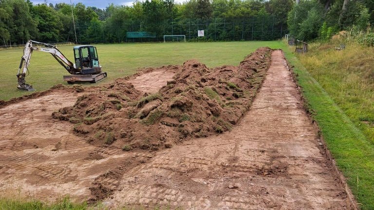 Ein Bagger gräbt Erde auf dem Fußballplatz ab, damit nach dem Auffüllen mit Schotter und Sand Boulebahnen entstehen können.