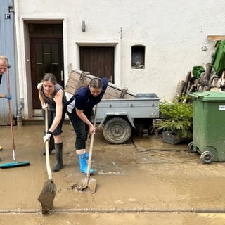 Anwohner und Helfer in Gummistiefeln schaben nach dem Hochwasser den Schlamm von einem Grundstück in Heidelsheim