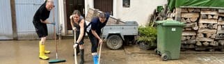 Anwohner und Helfer in Gummistiefeln schaben nach dem Hochwasser den Schlamm von einem Grundstück in Heidelsheim