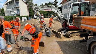 Mitarbeiter der Stadt Bruchsal helfen bei der Beiseitigung des Schlamms mit Bagger und Schaufeln. Das Unwetter im Kreis Karlsruhe hat Spuren hinterlassen. 