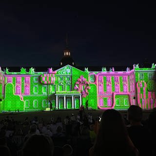 Die Fassade des Schlosses in Karlsruhe ist bei den Schlosslichtspielen 2024 in grell grünes und pinkes Licht getaucht.