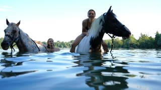 Frau badet mit Pferden in einem See