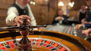 Ein Roulettetisch in einem Casino, im Hintergrund sind unscharf ein Croupier und ein Gast zu sehen.