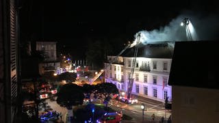 Aus dem Dachstuhl eines Hotels in Baden-Baden dringen im Jahr 2021 Rauchschwaden, während die Feuerwehr den Brand von Drehleitern aus bekämpft.