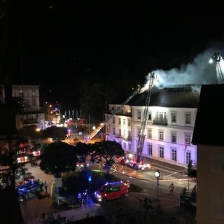 Aus dem Dachstuhl eines Hotels in Baden-Baden dringen im Jahr 2021 Rauchschwaden, während die Feuerwehr den Brand von Drehleitern aus bekämpft.