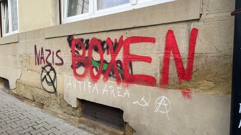 Auf einer Haus-Fassade steht der Text "Nazis boxen" und das Symbol mit Hammer und Sichel ist mit Sprühfarbe daneben gemalt.