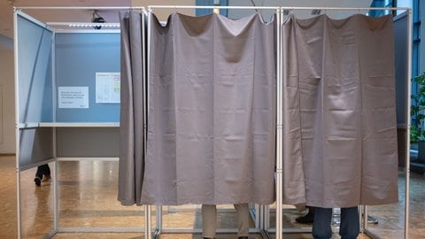 Symbolbild: Zwei Wählerinnen und ein Wähler füllen in einem Wahlbüro Wahlunterlagen aus. In Rastatt wird nach einer Panne neu gewählt.