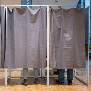 Symbolbild: Zwei Wählerinnen und ein Wähler füllen in einem Wahlbüro Wahlunterlagen aus. In Rastatt wird nach einer Panne neu gewählt.