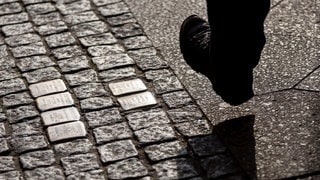 Symbolbild: Ein Mann geht an Stolpersteinen vorbei