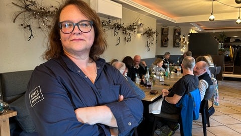 Stephanie Radtke steht im Essensraum ihres Restaurants, dem "Landgasthof zum Goldenen Anker", mit Blick zur Kamera vor einem Tisch mit Menschen.