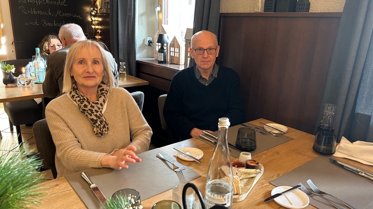 Ein Ehepaar sitzt in einem Restaurant auf Stühlen an einem gedeckten Tisch.