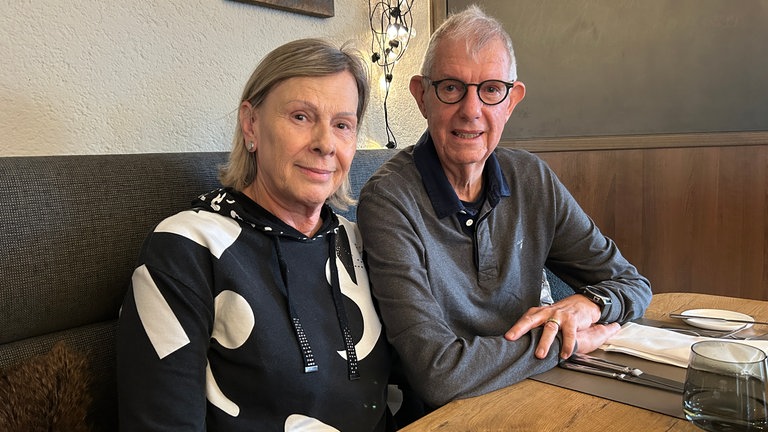 Eine Frau und ein Mann sitzen auf einer Sitzbank an einem gedeckten Tisch in einem Restaurant.