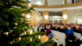 Gottesdienst an Weihnachten: Ein Strohstern hängt an einem Tannenbaum in einer Kirche