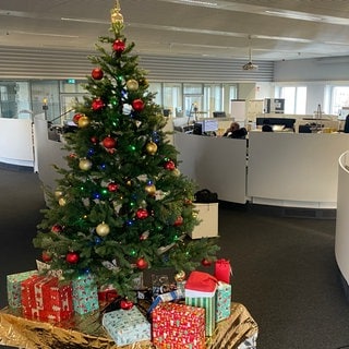 Ein bunt geschmückter Weihnachtsbaum, unter dem viele Geschenke liegen, steht im Büro der Notrufzentrale Karlsruhe.