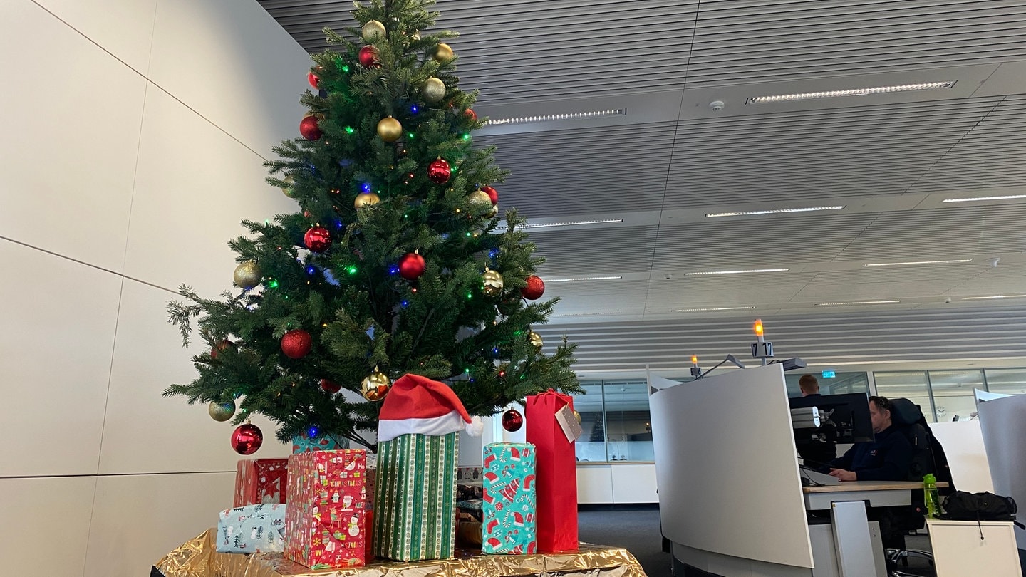 Ein bunt geschmückter Weihnachtsbaum, unter dem viele Geschenke liegen, steht im Büro der Notrufzentrale Karlsruhe.