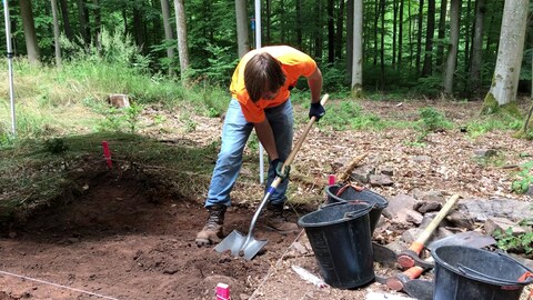 Ein junger Mann gräbt mit einer Schaufel im Waldboden 