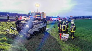 Feuerwehrleute stehen an einer Unfallstelle im Rhein-Neckar-Kreis neben einem schwer beschädigten Fahrzeug. 