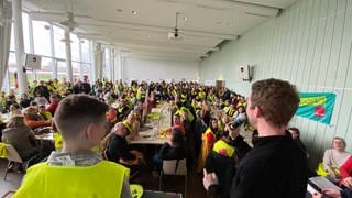 Streikende sitzen in gelben Westen an Tischen im Gewerkschaftshaus in Mannheim.