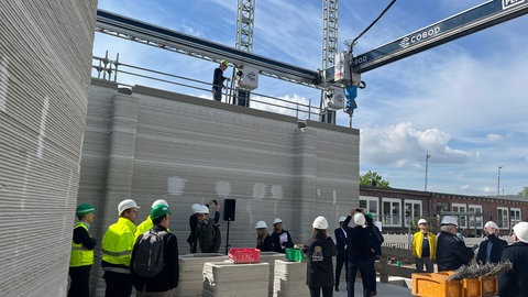 Beim Vor-Ort-Termin besichtigen Vertreter der Stadt und Journalisten die Baustelle mit dem 3D-Drucker für Zement