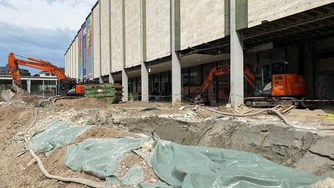 Vor dem Nationaltheater ist die Erde aufgerissen. Zwei große orange-farbene Bagger stehen auf dem Goetheplatz. 