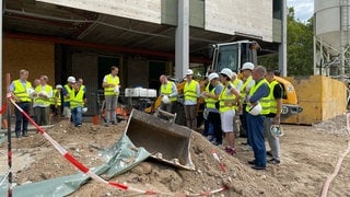 Der Mannheimer Oberbürgermeister Peter Kurz, der Intendant das Nationaltheaters Tilmann Pröllochs, Ministerialdirektor Hans J. Reiter und Mitglieder des Mannheimer Gemeinderats stehen neben einer Baggerschaufen auf der Baustelle vor dem Nationaltheater.