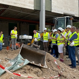 Der Mannheimer Oberbürgermeister Peter Kurz, der Intendant das Nationaltheaters Tilmann Pröllochs, Ministerialdirektor Hans J. Reiter und Mitglieder des Mannheimer Gemeinderats stehen neben einer Baggerschaufen auf der Baustelle vor dem Nationaltheater.