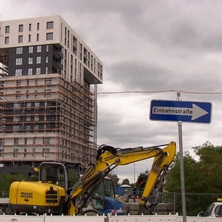 Ein Bagger steht vor einem Hochhaus mit Baugerüst.