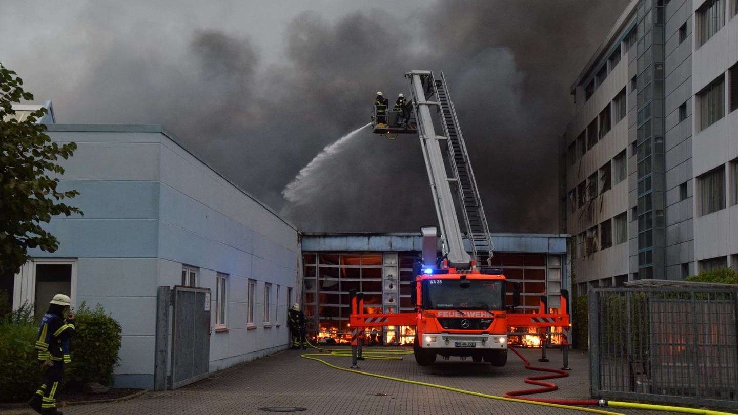 Feuer und Rauchwolken sowie Feuerwehrauto vor Fabrikhalle