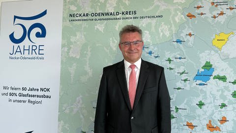 Der Landrat des Neckar-Odenwald-Kreises, Achim Brötel, steht vor einer Karte des Landkreises.