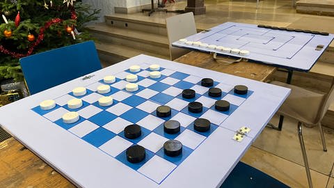 Ein Schach- und ein Mühlespiel liegen auf Tischen, im Hintergrund steht ein geschmückter Weihnhachtsbaum.