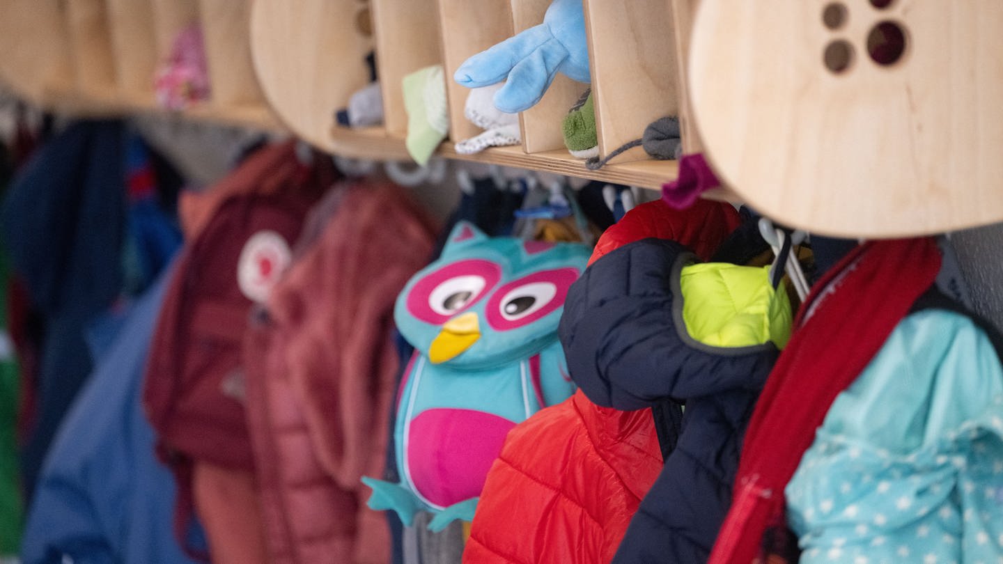 An einer Garderobe in einer Kita hängen Jacken und Kinderrucksäcke.
