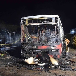 Ein komplett ausgebrannter Bus steht vor einem Hotel, die Partyzelte im Hintergrund sind ebenfalls ausgebrannt und schwarz.