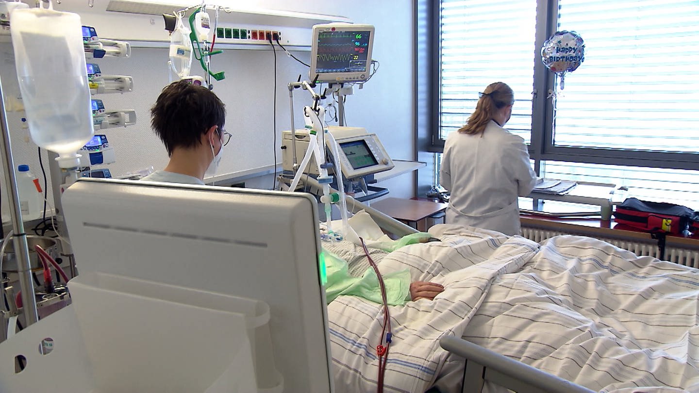 Zwei Krankenpflegerinnen kümmern sich um einen Patienten im Krankenhausbett.