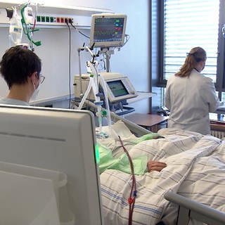 Zwei Krankenpflegerinnen kümmern sich um einen Patienten im Krankenhausbett.