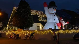 Geschmücktes Weihnachtshaus mit Lichtern und Riesenschneemann und Weihnachtsmann im Vorgarten