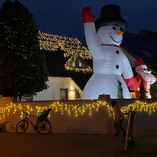 Geschmücktes Weihnachtshaus mit Lichtern und Riesenschneemann und Weihnachtsmann im Vorgarten