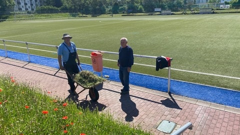 Zwei Männer mit Schubkarre neben dem Fußballfeld