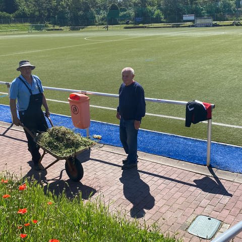 Zwei Männer mit Schubkarre neben dem Fußballfeld