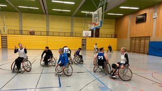 Mehrere Menschen im Rollstuhl spielen in einer Sporthalle Basketball.