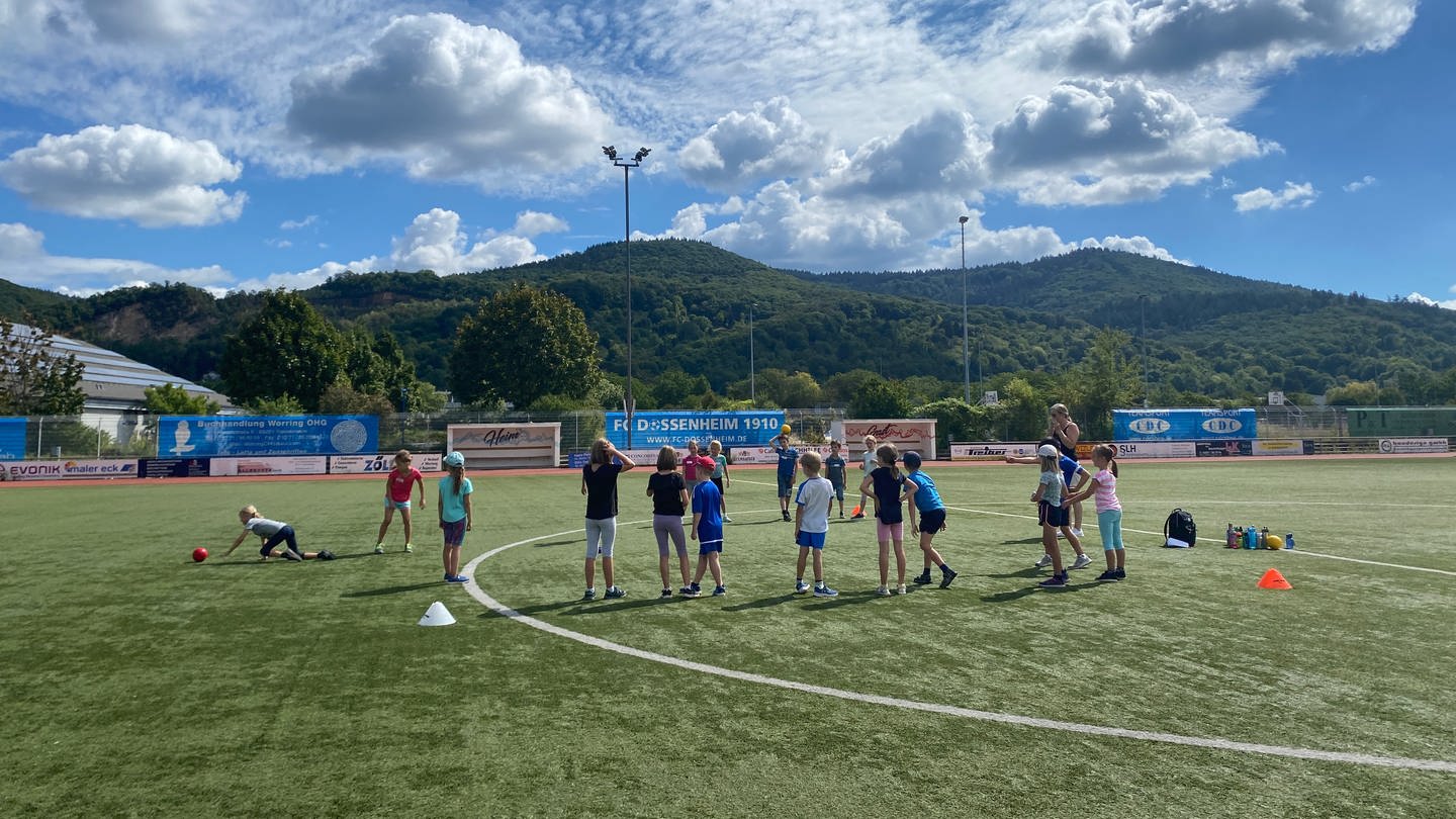 Die Kinder toben sich beim Sommerferien-Camp in Dossenheim (Rhein-Neckar-Kreis) ordentlich aus. Auf dem Sportplatz wird zum Beispiel Brennball gespielt.