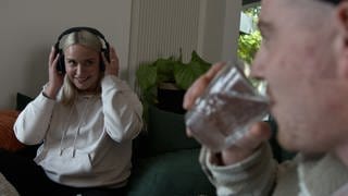 Theresas Freund trinkt, während sie Kopfhörer trägt und somit das Geräusch besser ertragen kann.