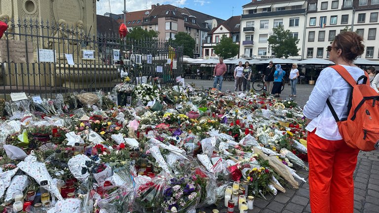 Blumen und Sträuße vor dem Brunnen auf dem Mannheimer Marktplatz, Frau steht daneben und trauert